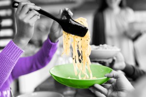 Hands using a pair of utensils to lift a bunch of pasta