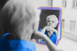 Older female with gray hair and wrinkles looking in mirror