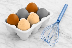 Metal whisk placed next to a carton of six eggs