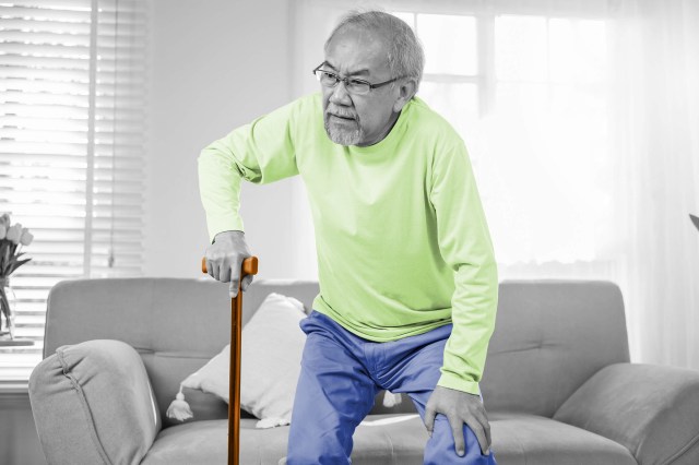 Elderly man using a cane to stand up from a sofa