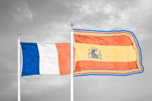 France and Spain flags against a cloudy sky