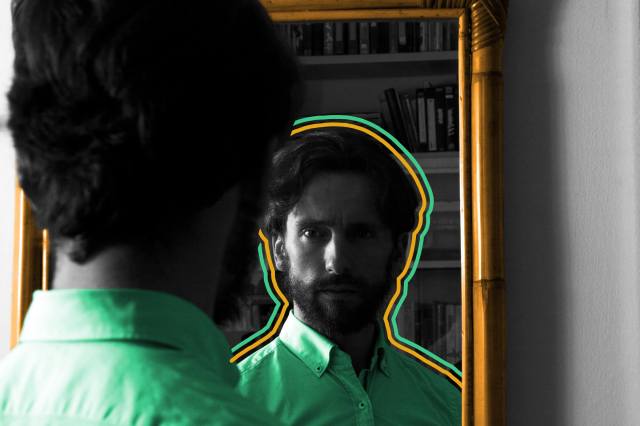 Man staring at his reflection in a dimly lit mirror